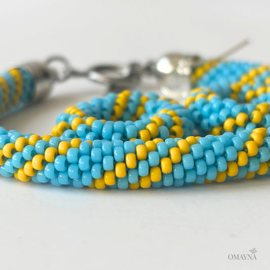 Close-up of a blue and yellow beaded bracelet and earings on a white background | Cala set