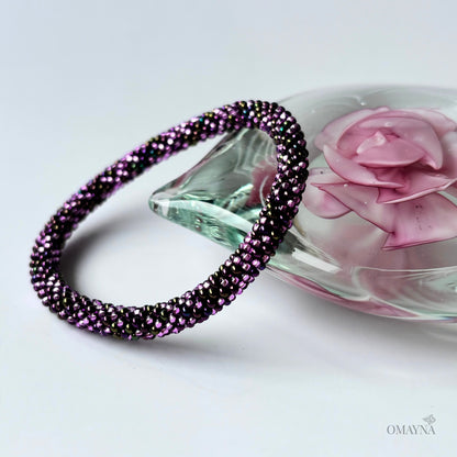 Purple beaded bracelet on a white surface with a pink rose and crystal object in the background.
