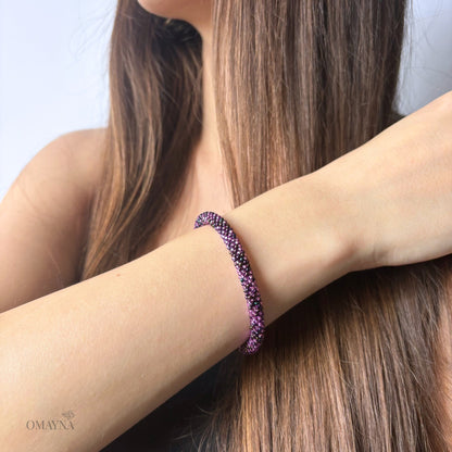 Close-up of a person wearing a purple beaded bracelet with a neutral background