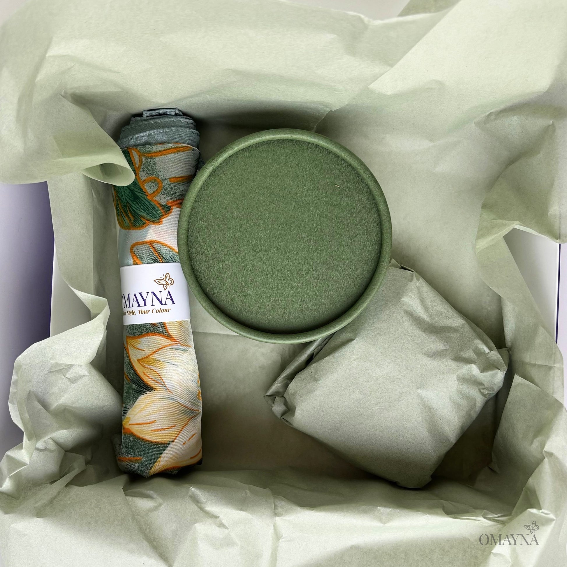 Product set with a green container, silk scarf, and artisan soap in a gift box with wrapping