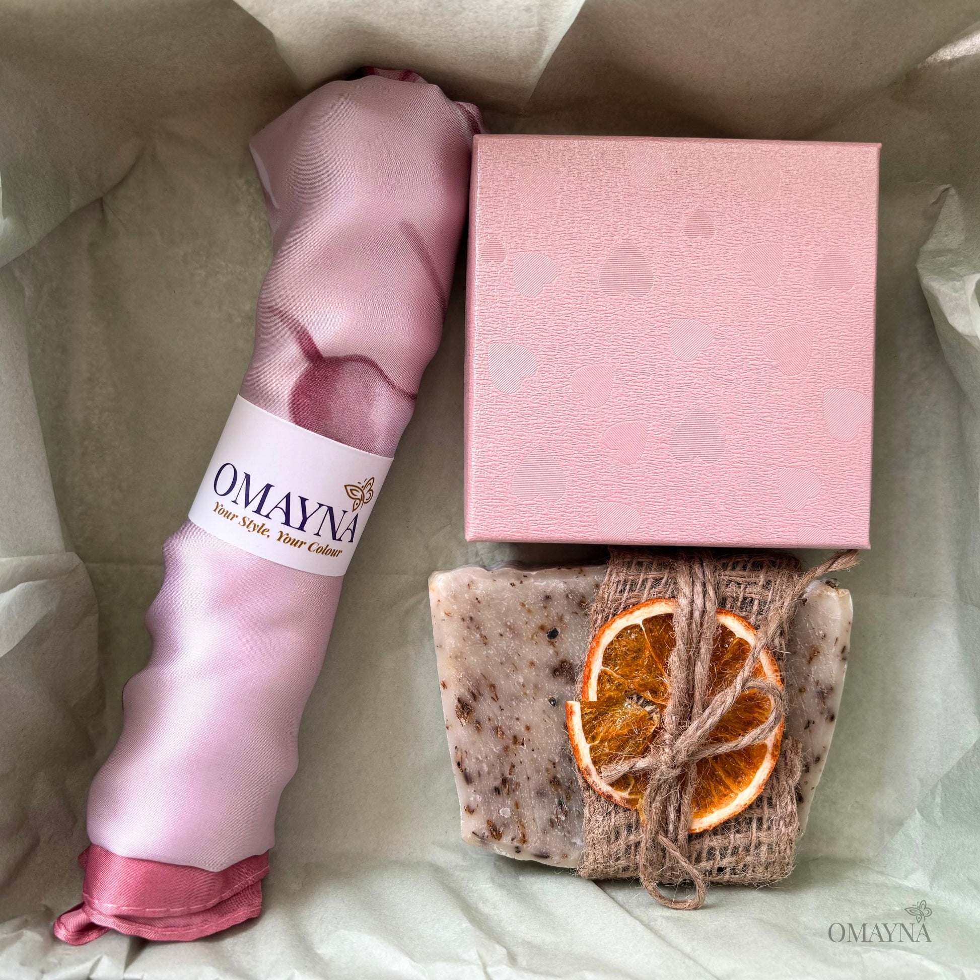 Pink scarf, soap with orange slices, and pink box on a light background