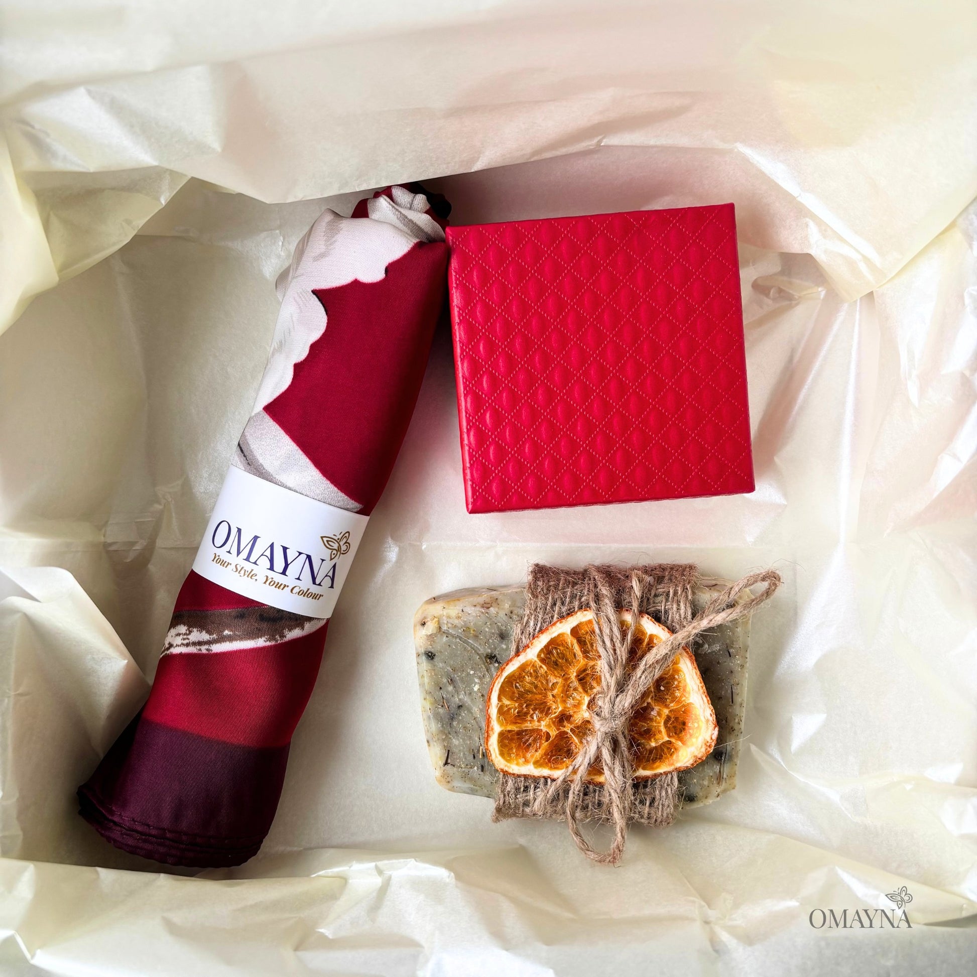 Gift set with red silk scarf, artisan soap, and dried oranges, gift box in red on a white background