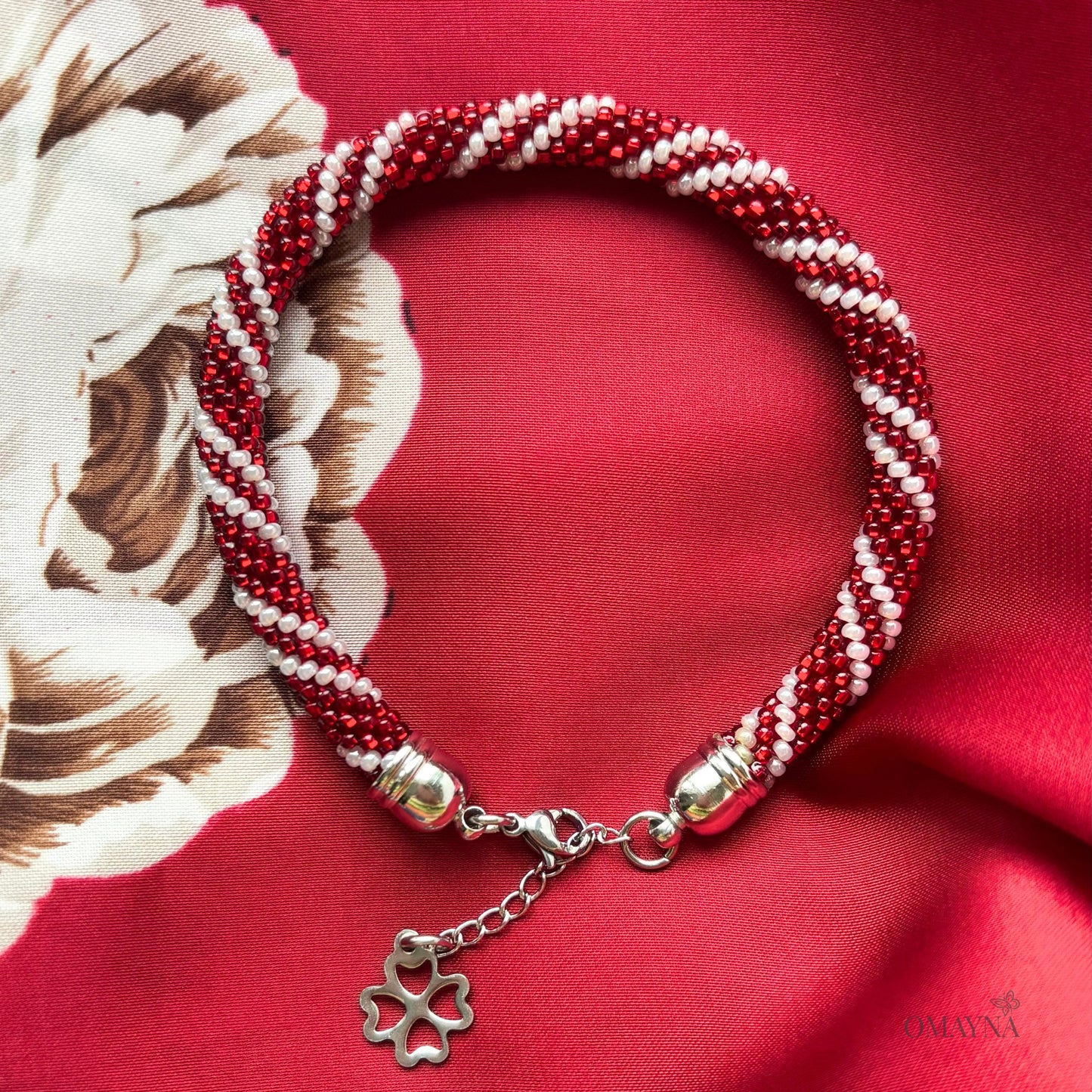 Red and pearl beaded bracelet with a silver clover charm on a red fabric background