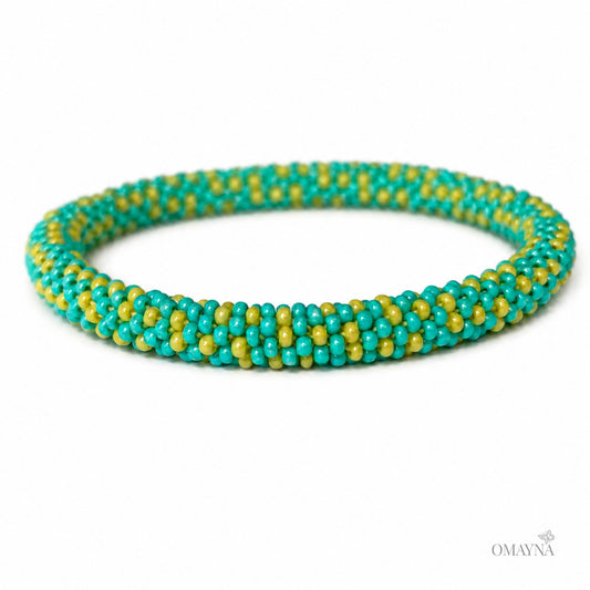 A beaded bracelet with a pattern of turquoise blue and lime green beads, displayed on a clean white background with a small OMAYNA logo in the bottom right corner.