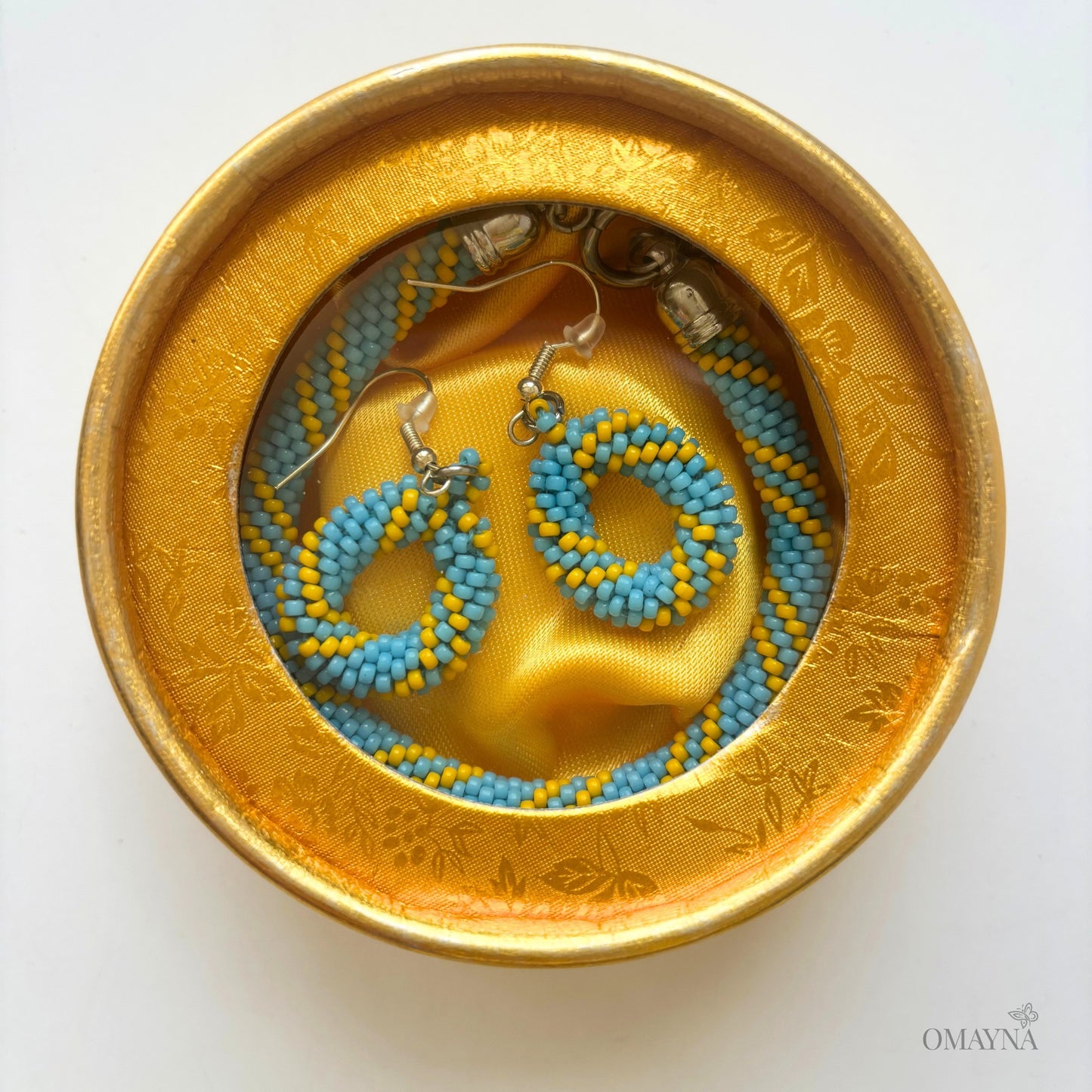 Pair of beaded earrings and a bracelet in a gold jewellery box | Cala set Omayna