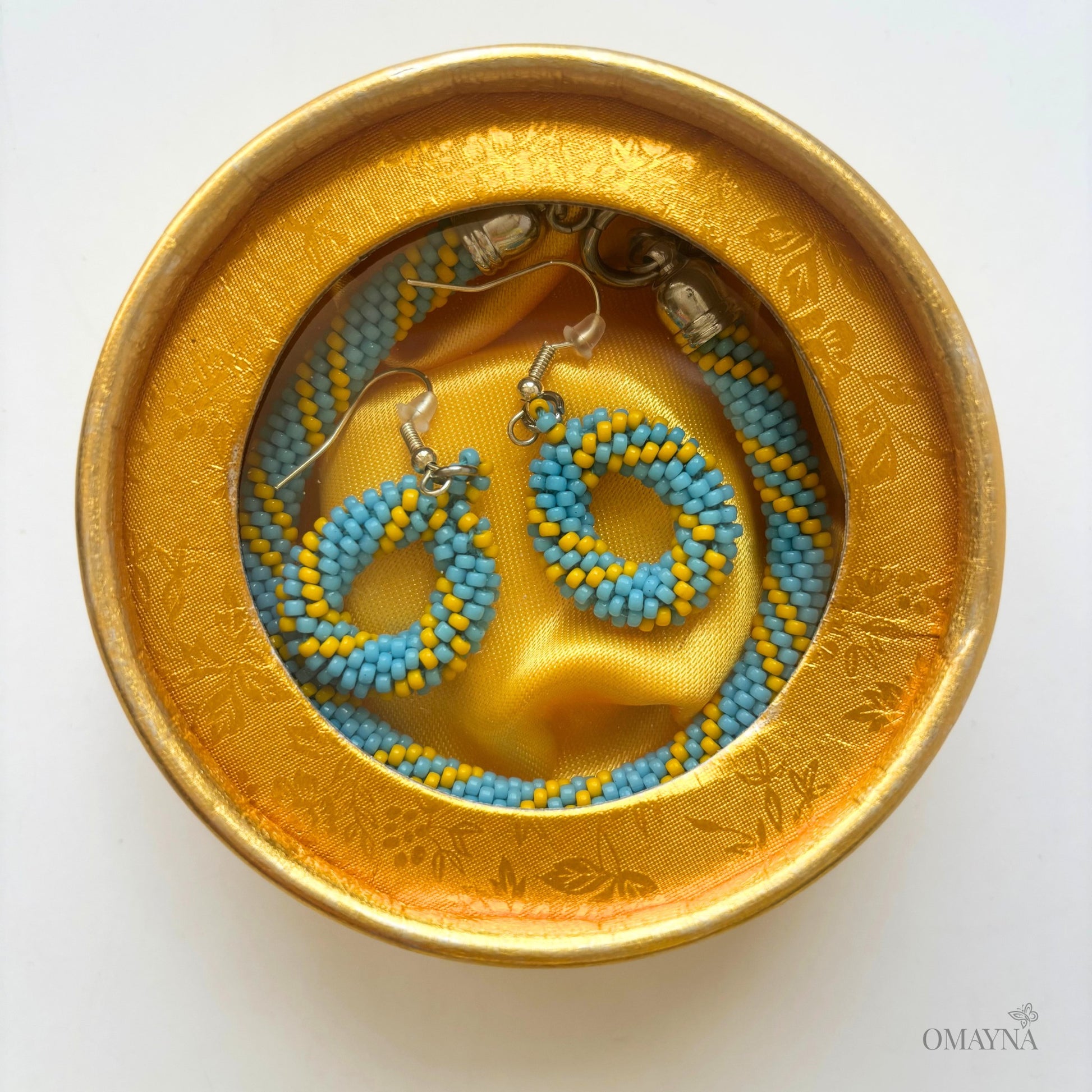 Pair of beaded earrings and a bracelet in a gold jewellery box | Cala set Omayna
