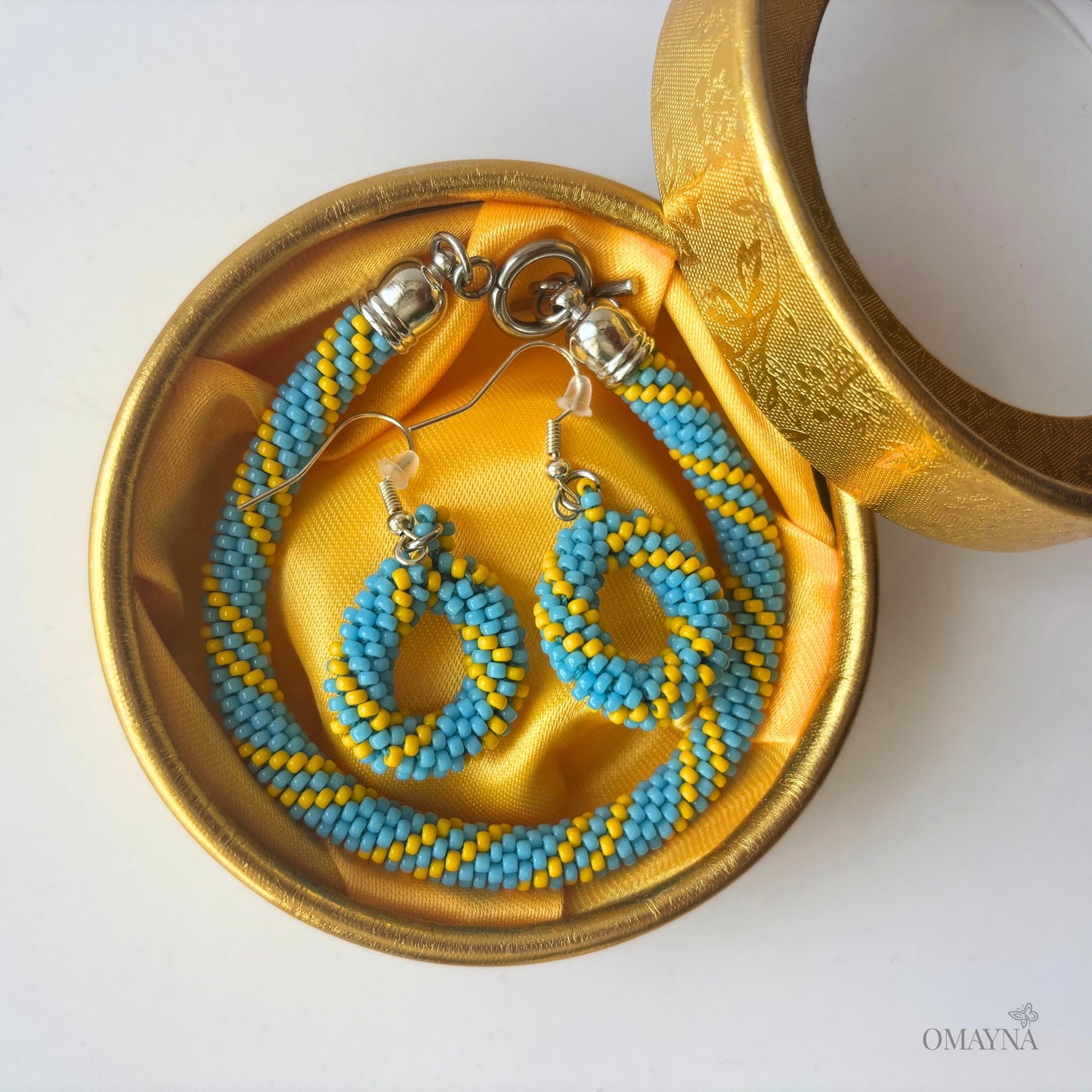 Blue and yellow beaded earrings and bracelet in a gold jewellery box on a white background | Omayna Cala set