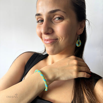 Woman wearing colourful earrings and a bracelet, with a plain background - Omayna Cala set in light blue & yellow