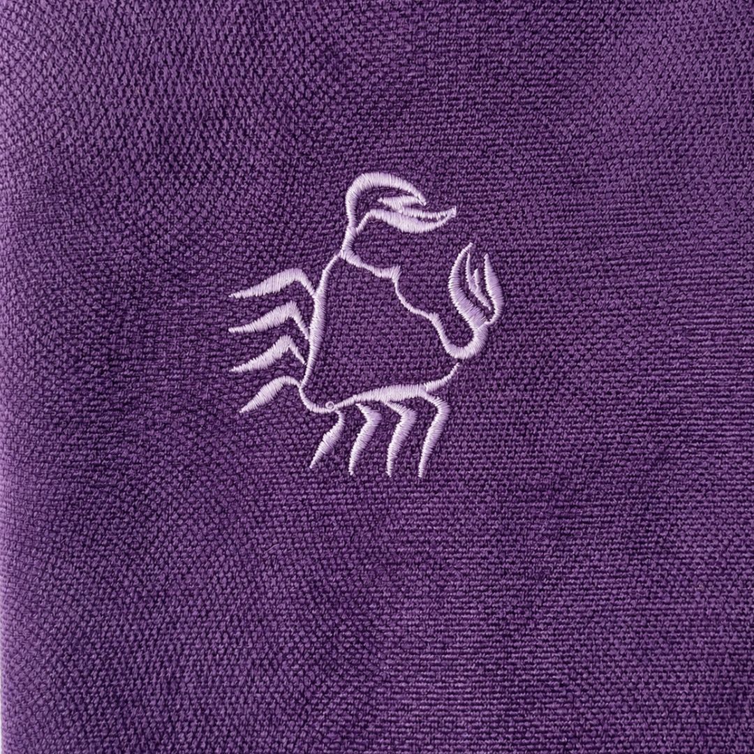 A close-up of a purple textured fabric featuring an embroidered light purple Cancer sign design in the center.