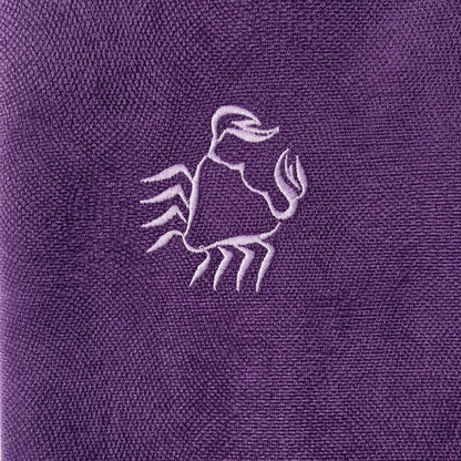 A close-up of a purple textured fabric featuring an embroidered light purple Cancer sign design in the center.