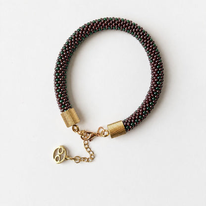 A beaded bracelet with dark green and brown beads, gold-toned textured end caps, a lobster clasp, and a dangling gold chain with a small charm of Cancer sign from the Zodiac, shown on a plain white background.