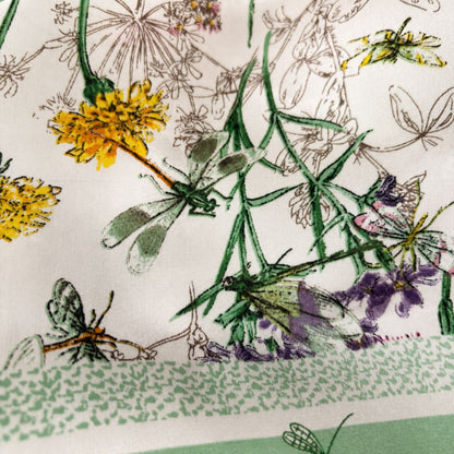 A close-up of a printed fabric featuring delicate botanical and insect motifs, including green dragonflies, yellow flowers, purple blossoms, and fine line-drawn wildflowers on an off-white background.