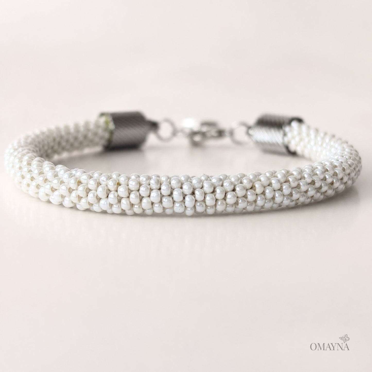 Pearl bracelet with silver clasp on a light background, featuring the brand 'OMAYNA'.