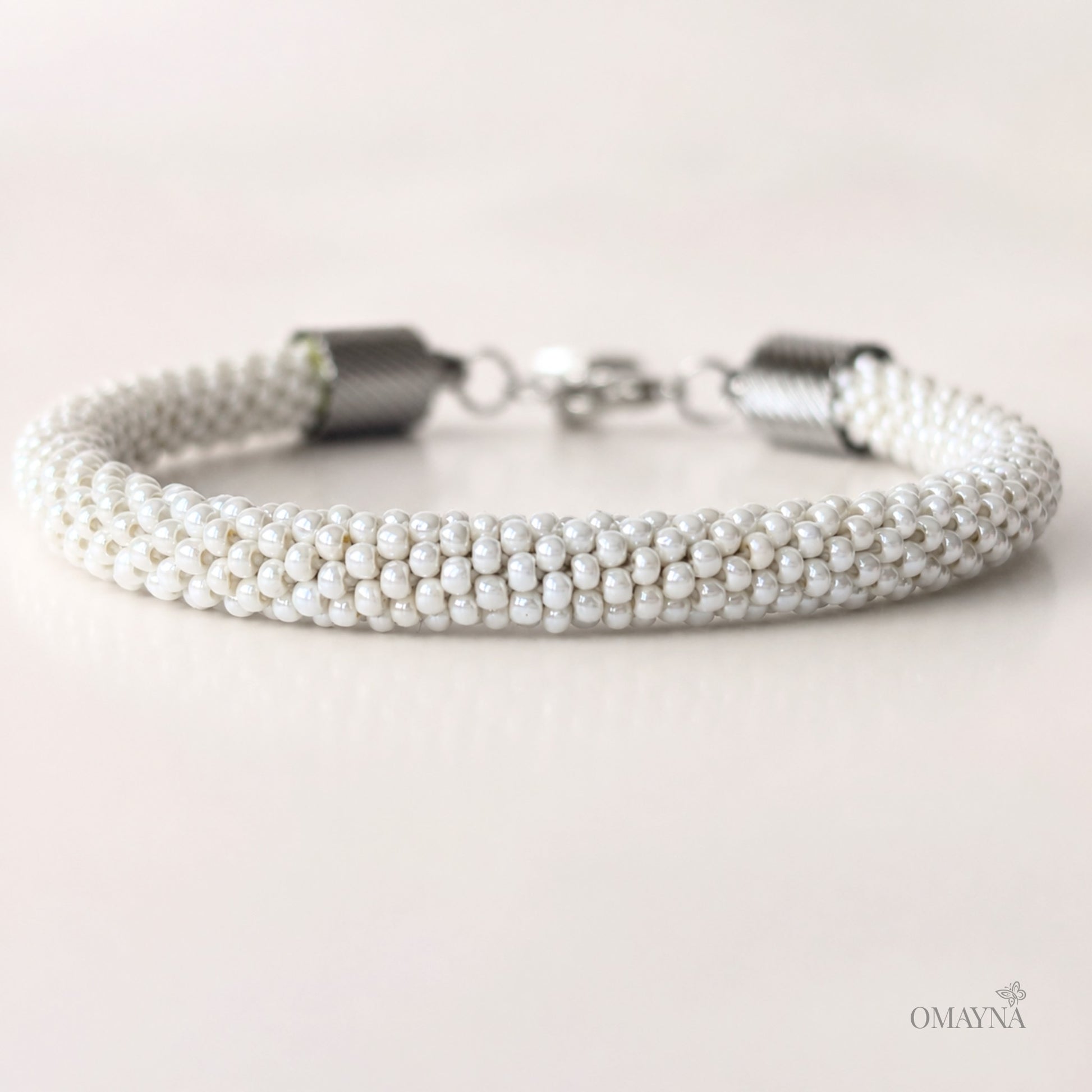 Pearl bracelet with silver clasp on a light background, featuring the brand 'OMAYNA'.