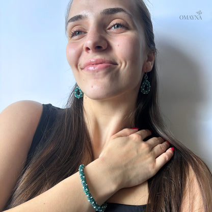Woman wearing green earrings and bracelet - Omayna Ivy set, smiling against a plain background