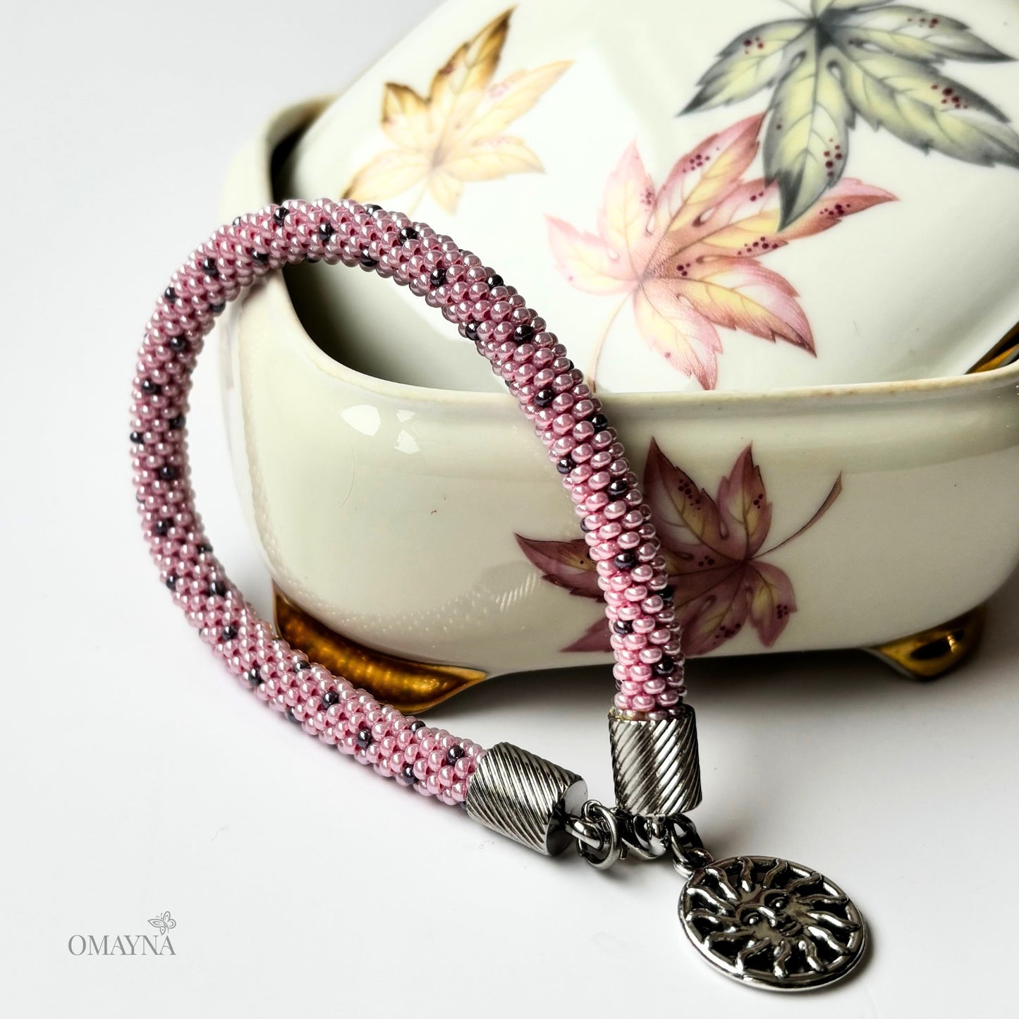 Lina Pink beaded bracelet with a silver charm on a white surface with a floral jewellery box in the background.