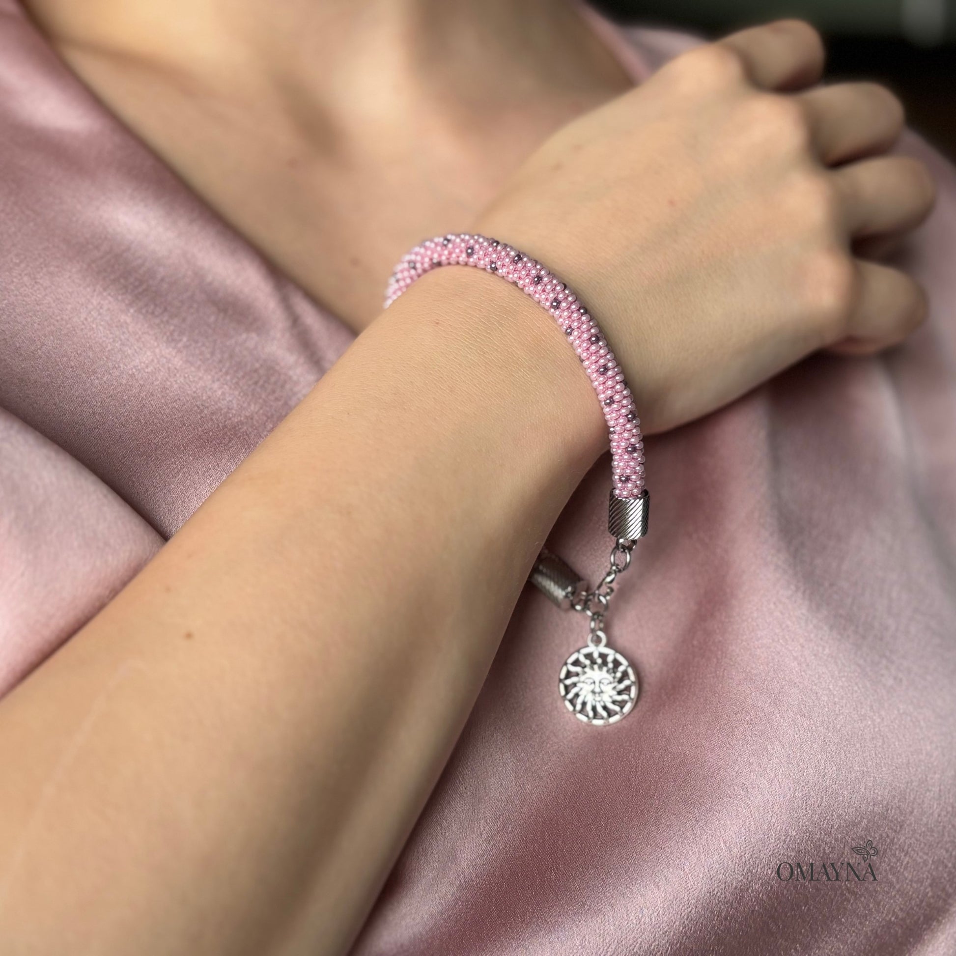Lina Pink beaded bracelet with a silver charm on a young girl's wrist, pink blouse on the background