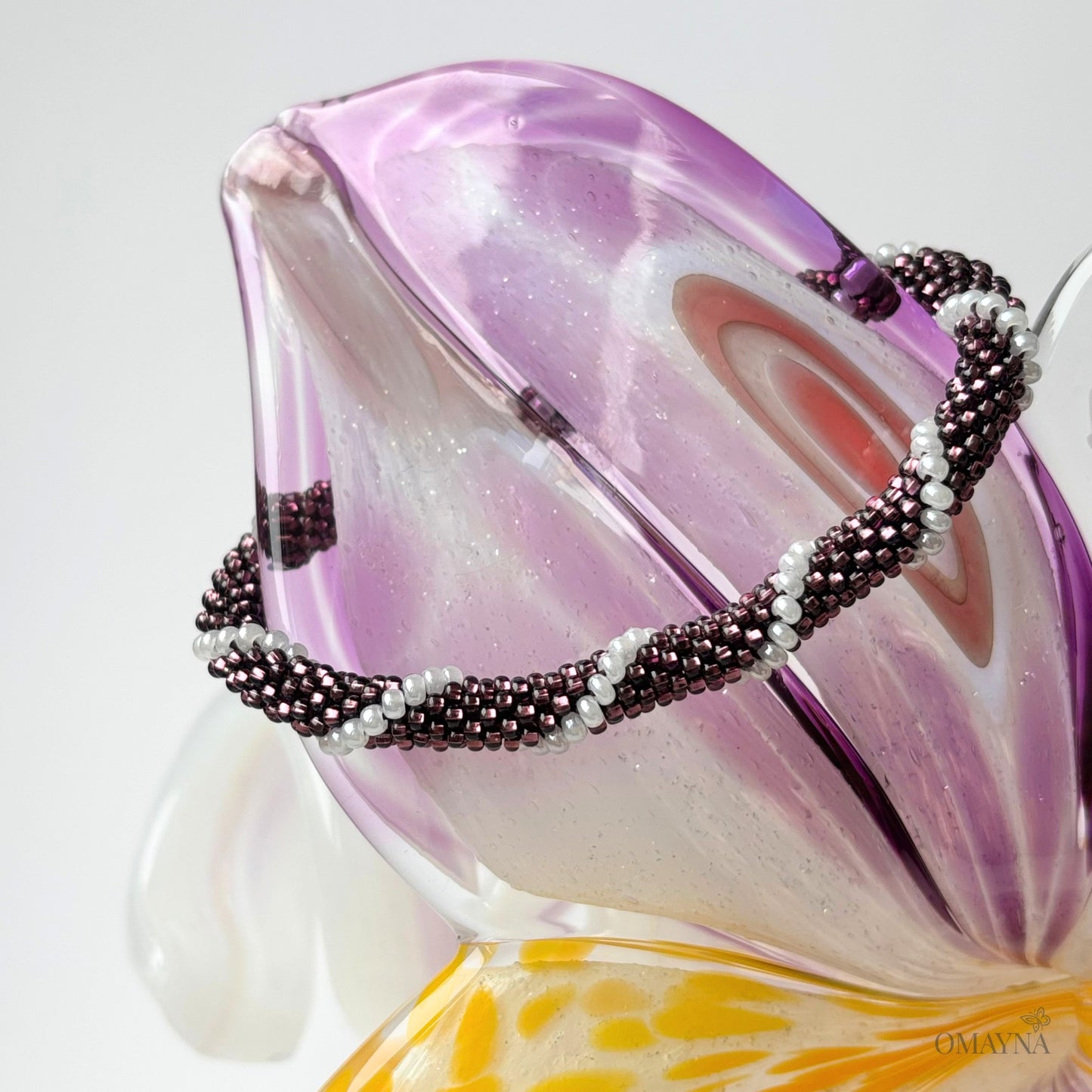 Beaded bracelet in purple and white on a decorative glass object with floral design