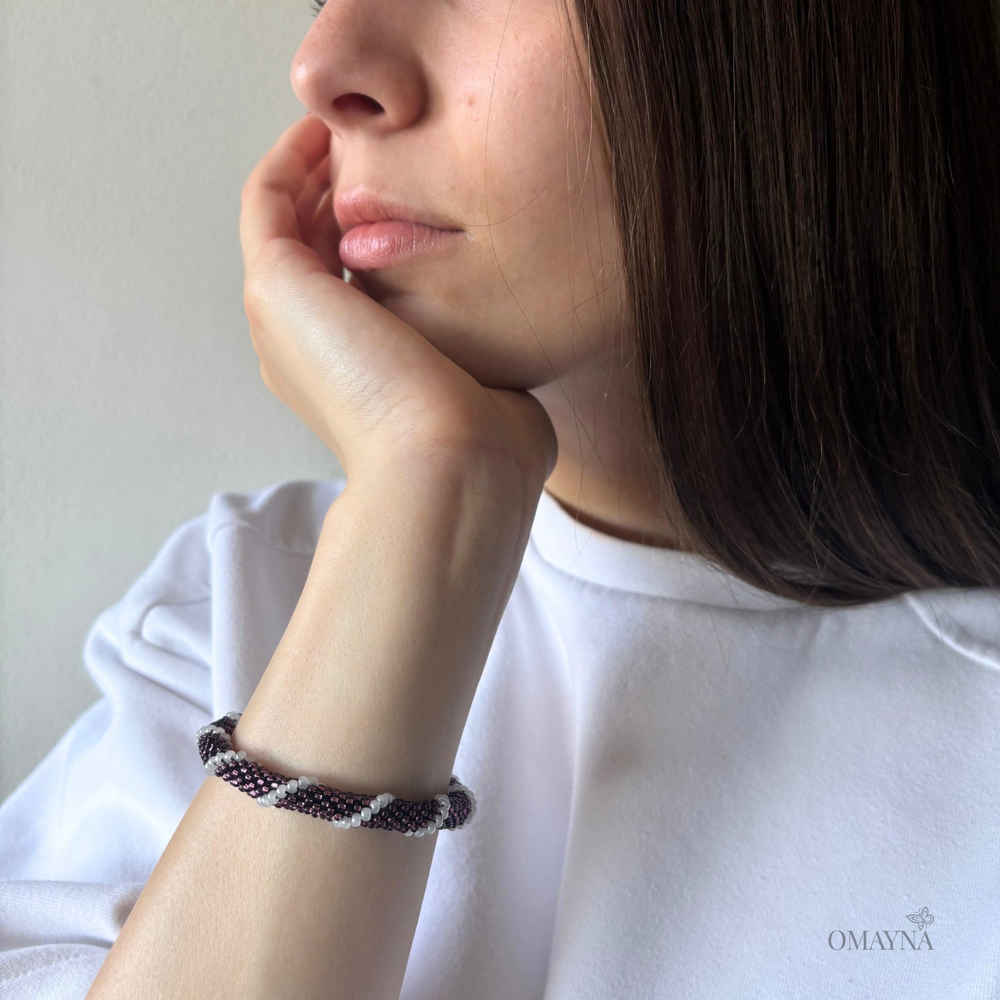 Person wearing a bracelet in purple & pearl with a neutral background