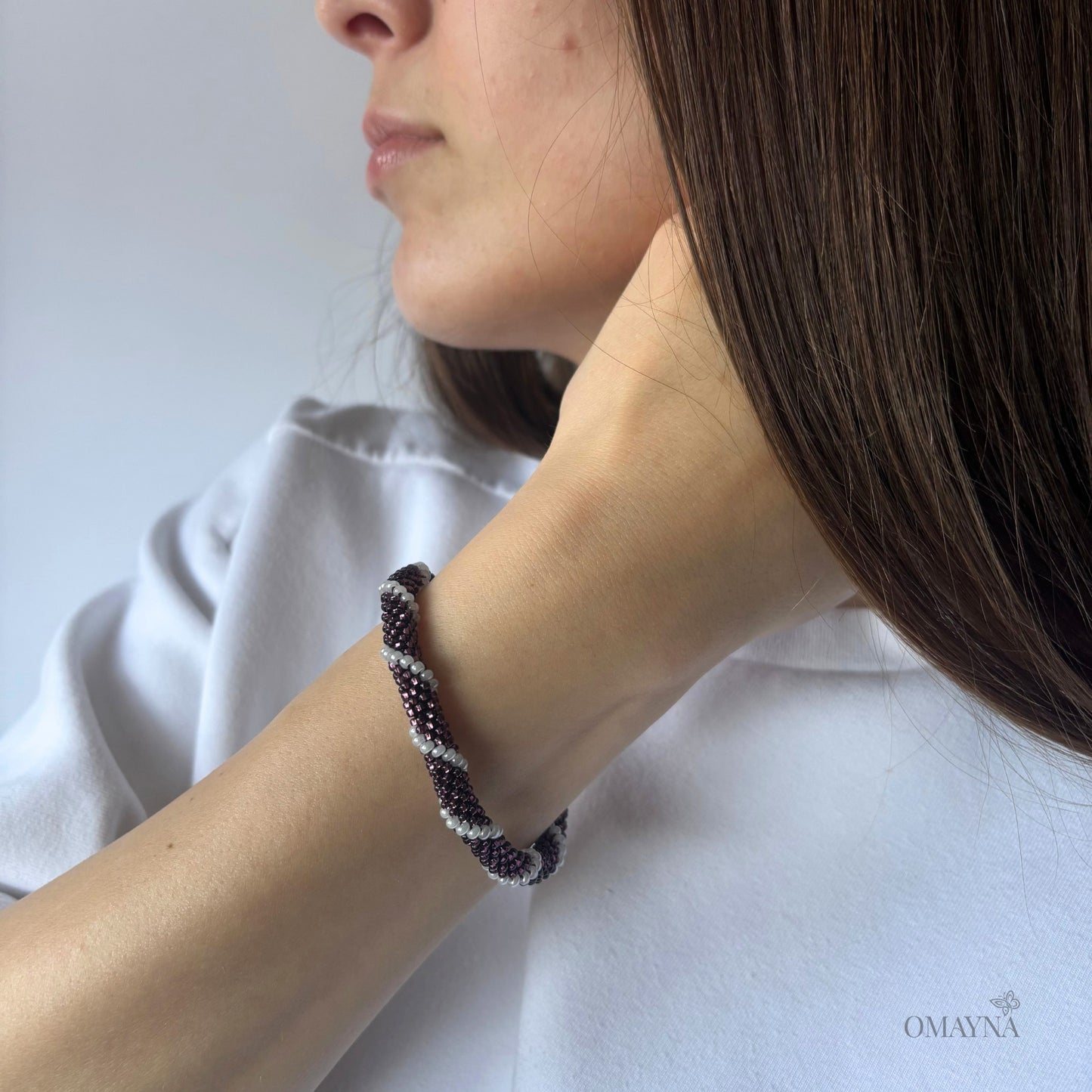 Person wearing a bracelet in purple & pearl with a neutral background