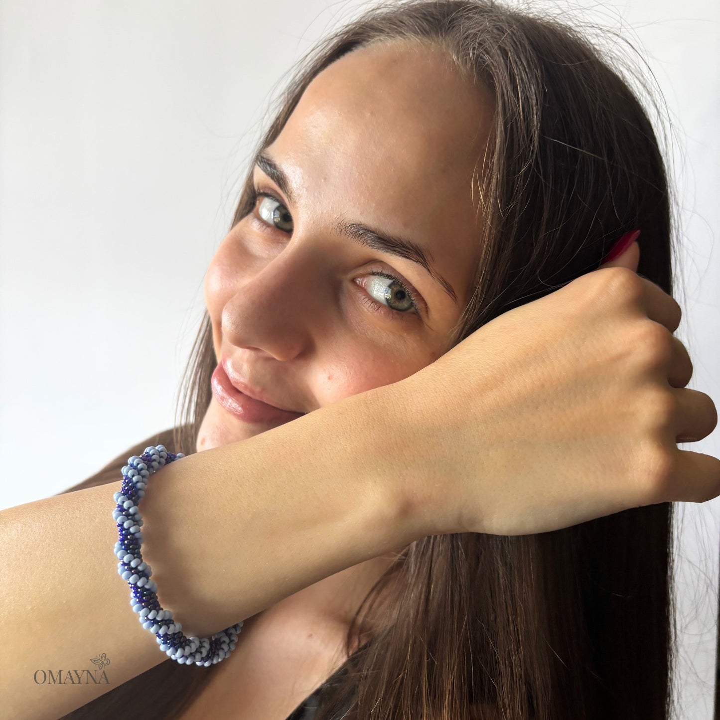 Woman with a blue beaded bracelet on her wrist, posing with her hand near her face.
