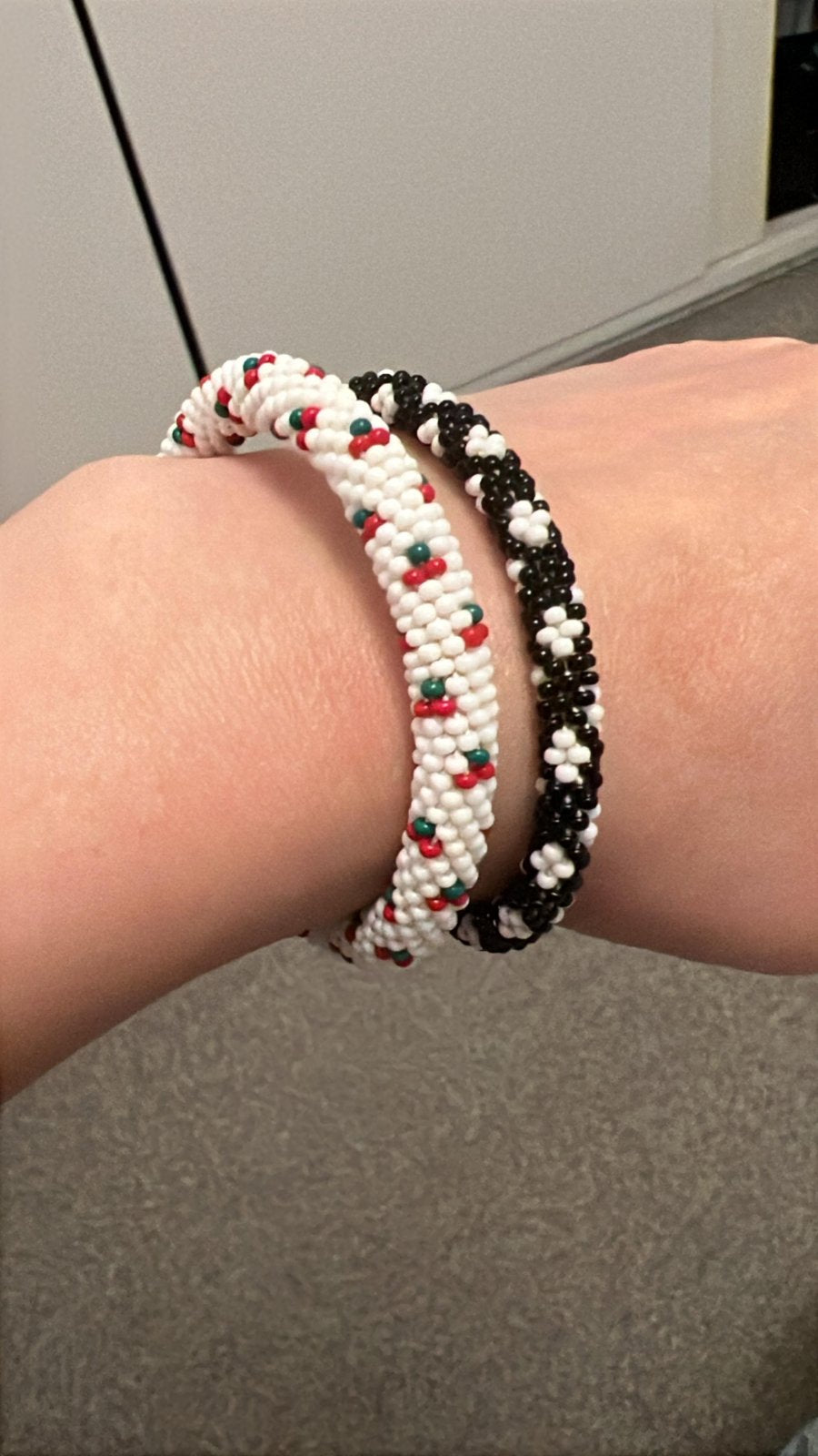Two beaded bracelets on a hand, background in gray