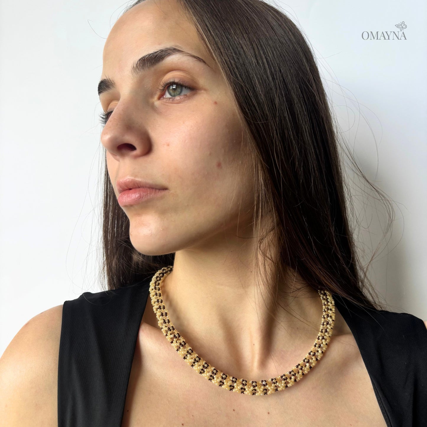 Woman wearing a necklace in beige & brown against a plain background
