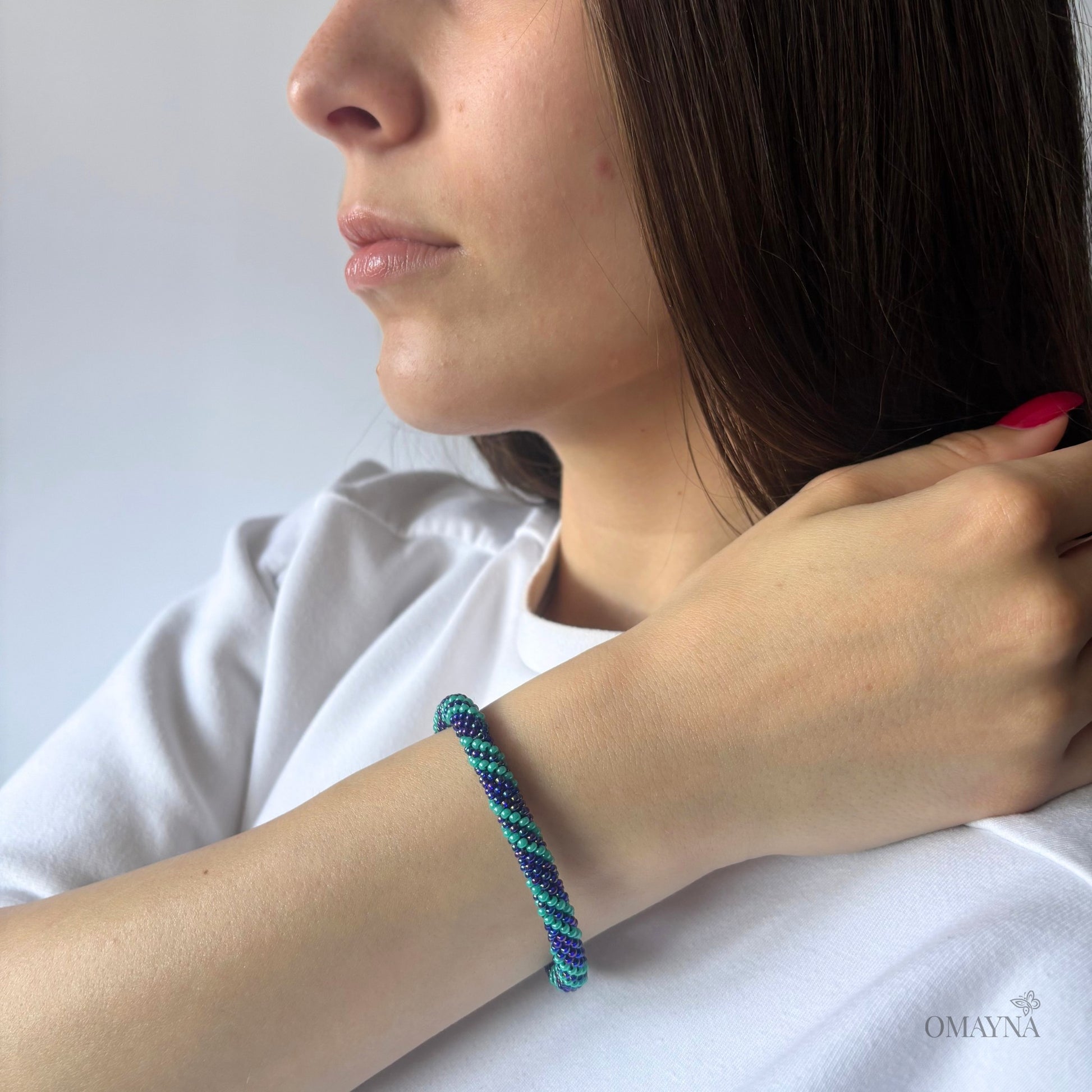 Close-up of a person wearing Nadya colorful beaded bracelet on a plain background