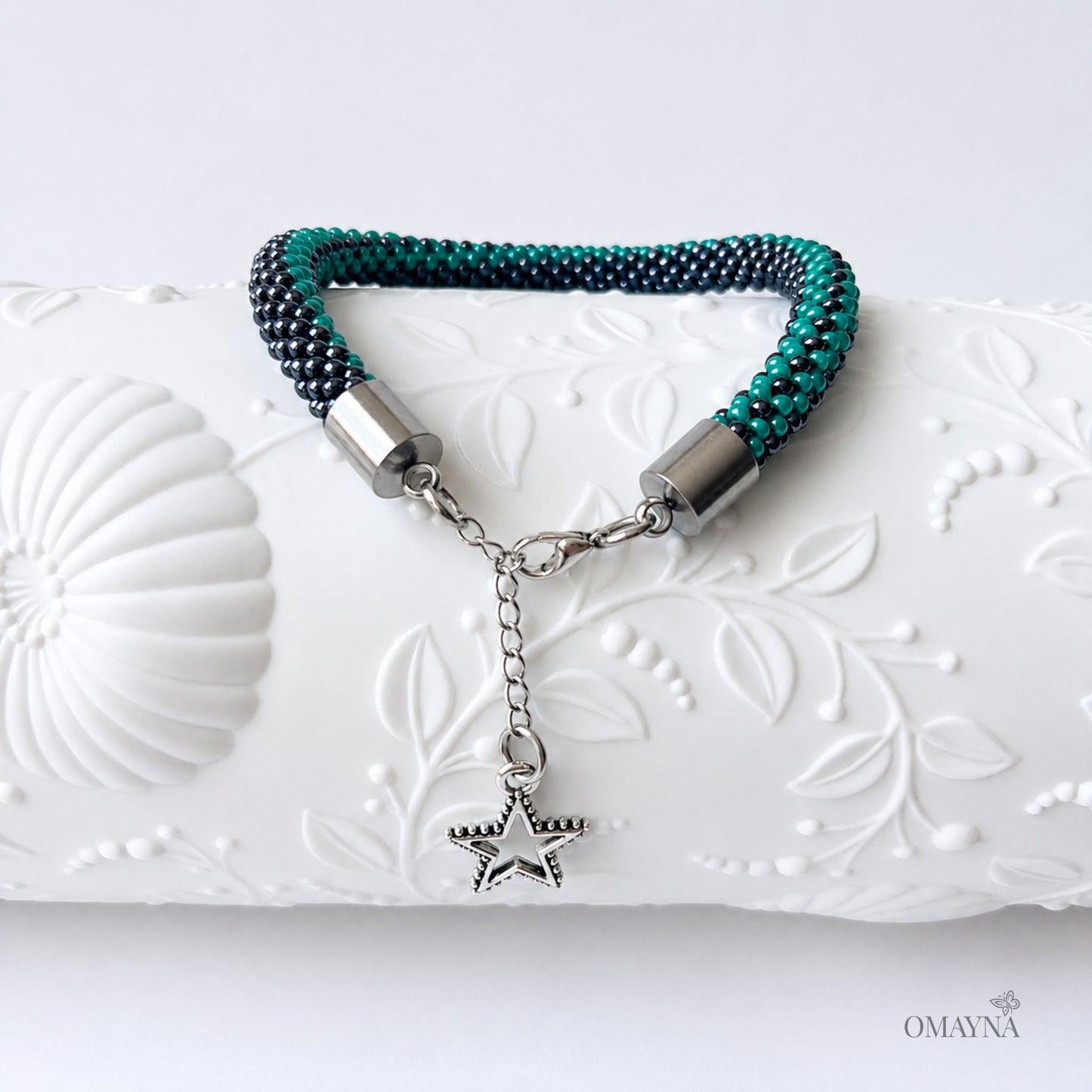 Bracelet with star charm on a decorative white surface, featuring the brand 'OMAYNA'.