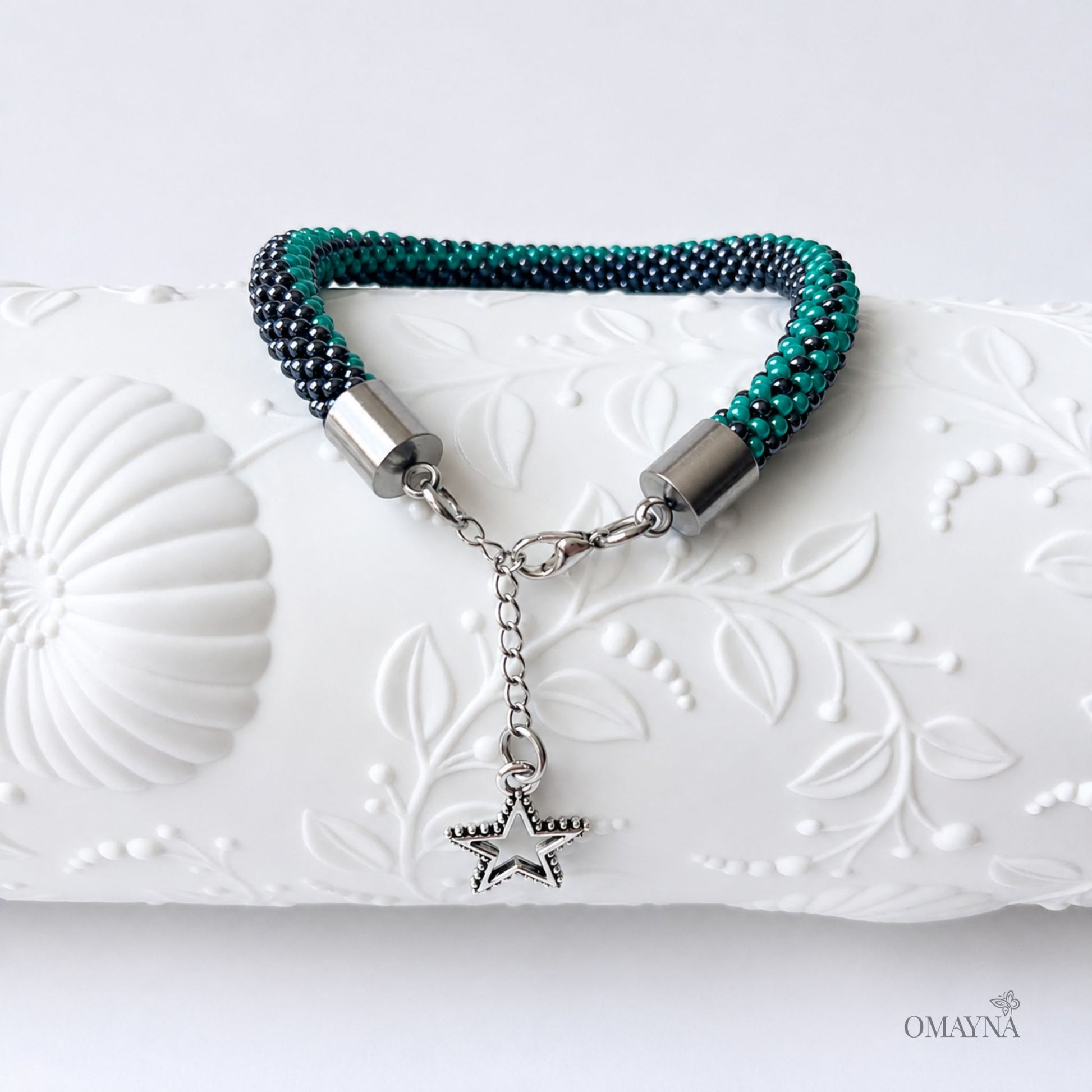 Bracelet with star charm on a decorative white surface, featuring the brand 'OMAYNA'.