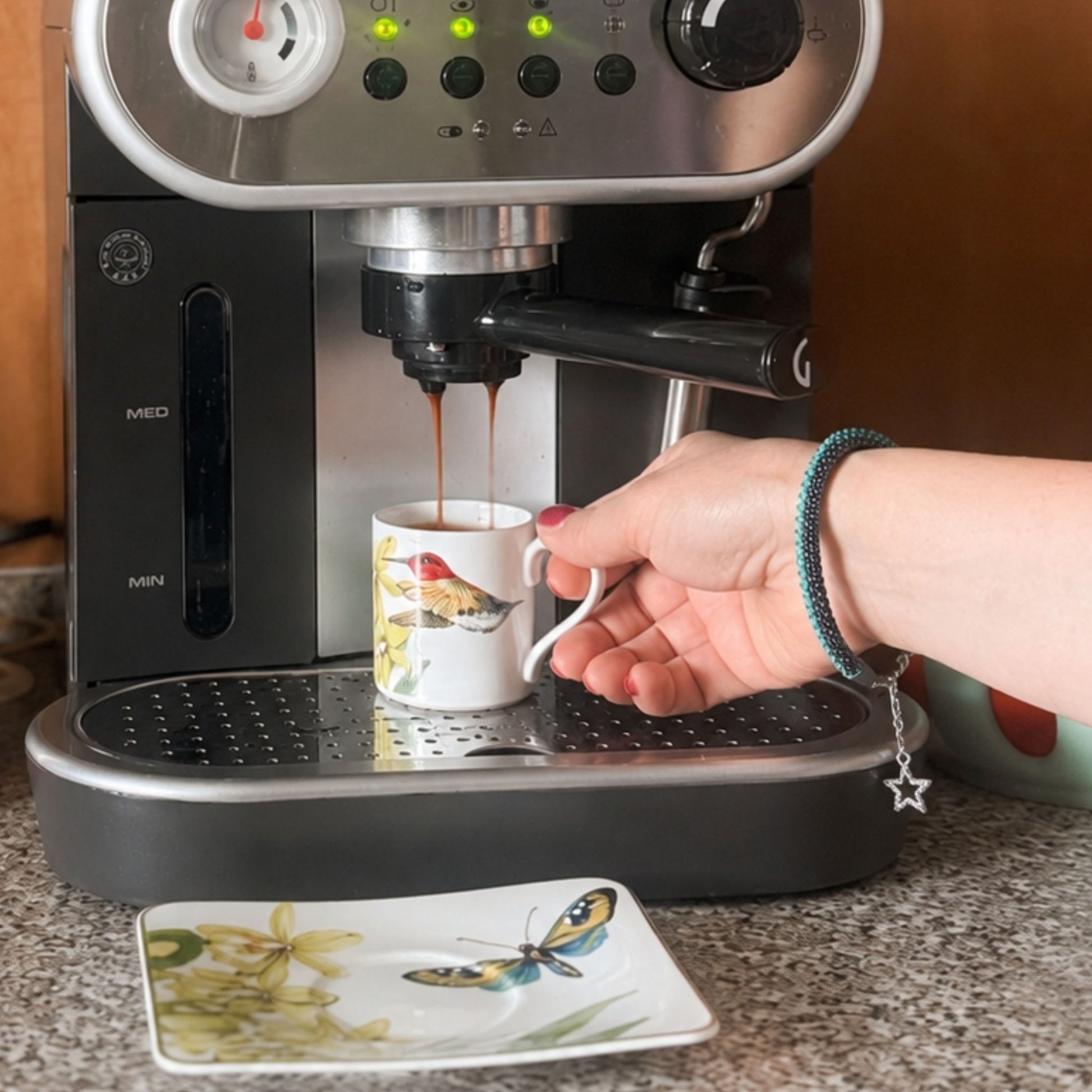 Espresso machine dispensing coffee into a cup held by a person wearing a bracelet with a silver star charm