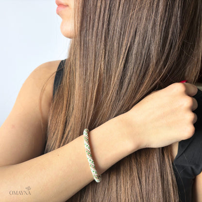 Person with long brown hair wearing a green and pearl beaded bracelet on a light background