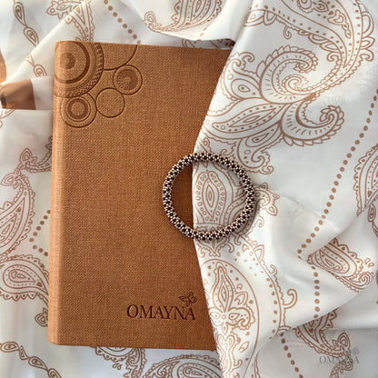Beaded bracelet in beige and brown, Brown notebook with embossed design and 'OMAYNA' branding on a patterned silk scarf background