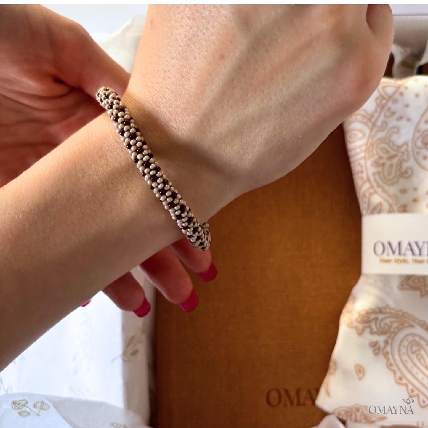 Close-up of a hand wearing a beaded bracelet with a branded box in the background