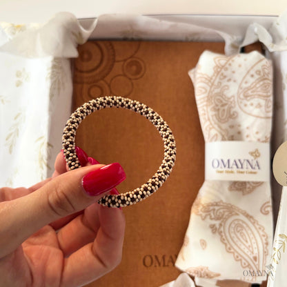 Hand holding a beaded bracelet with a branded box in the background