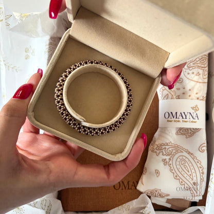 Hand holding a beaded bracelet in a beige box with Omayna branding.