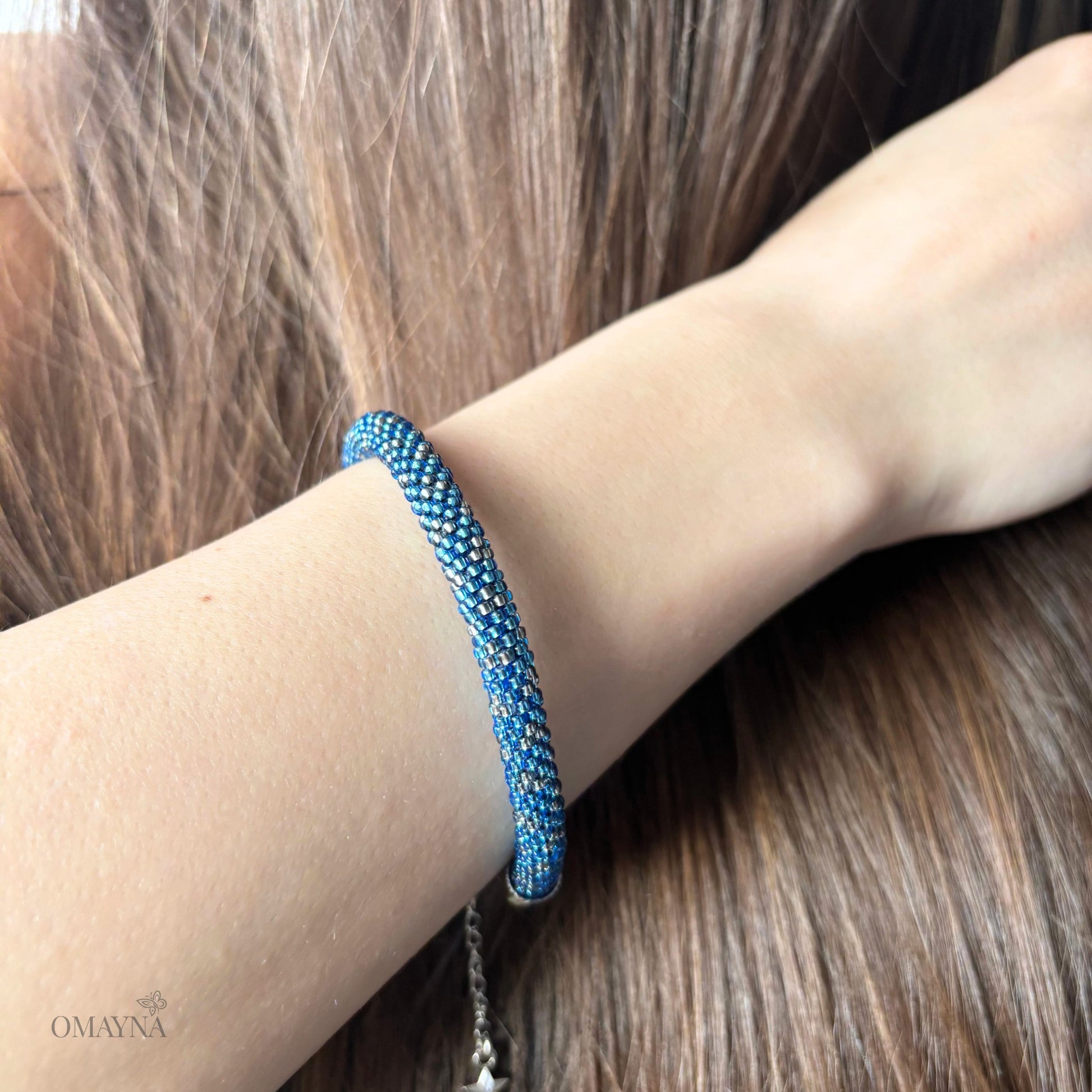 Blue and silver beaded bracelet on a wrist with blurred hair in the background