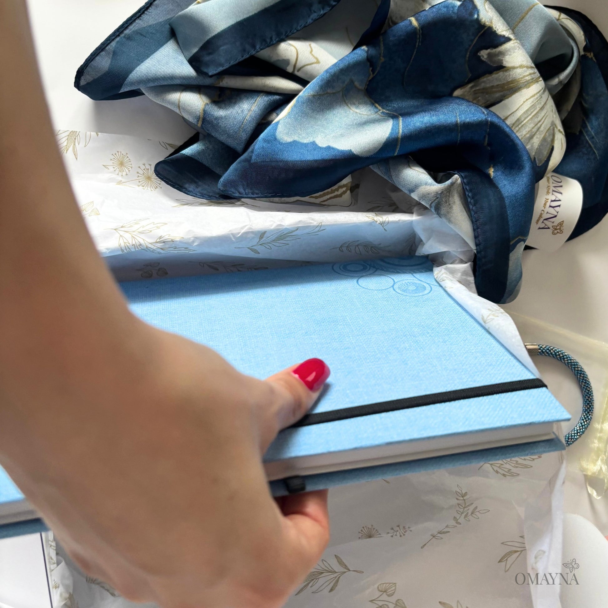 Hand holding a blue notebook with a patterned silk scarf background
