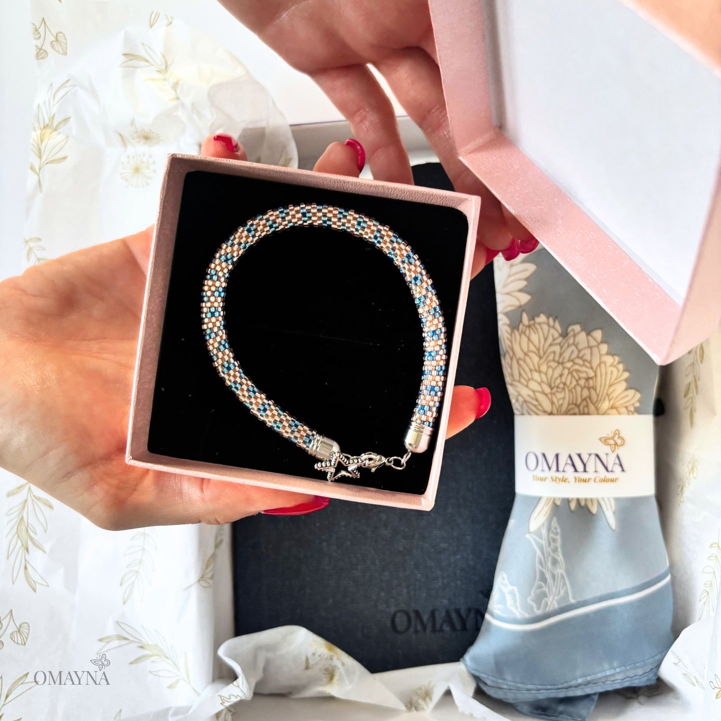 Bracelet in a pink box held by a person with a 'Omayna' branded background