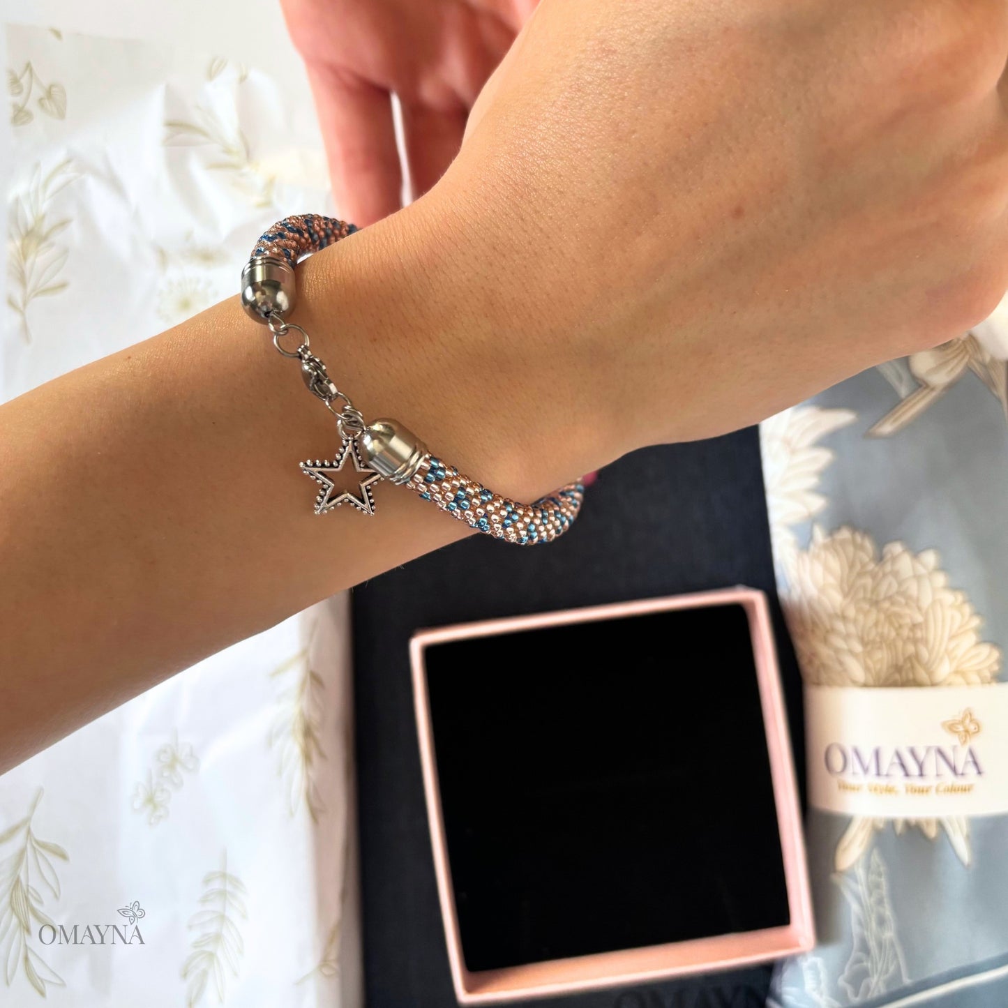 Bracelet with star charm on wrist next to Omayna packaging
