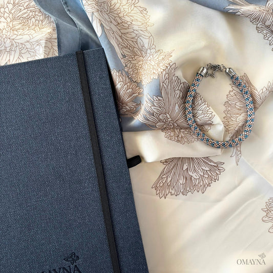 Blue notebook and bracelet in blue and light pink on a floral-patterned silk scarf with Omayna branding.