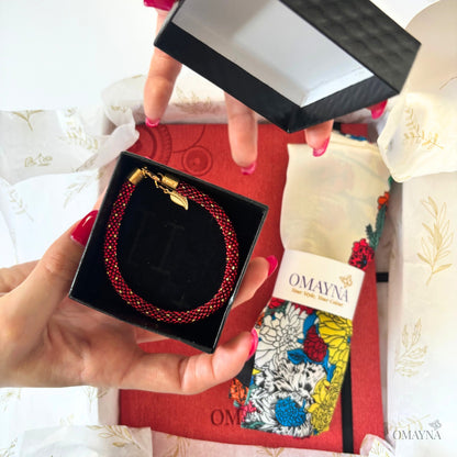 hands showing a bracelet in a box, notebook set in crimson - bracelet in a black gift box, scarf with floral motif and red notebook, all in a gift box