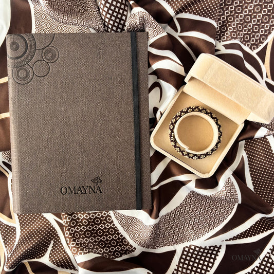 Brown notebook with 'OMAYNA' branding with a bracelet on a scarf