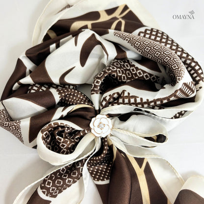 Brown and white patterned scarf with a decorative button on a light gray background