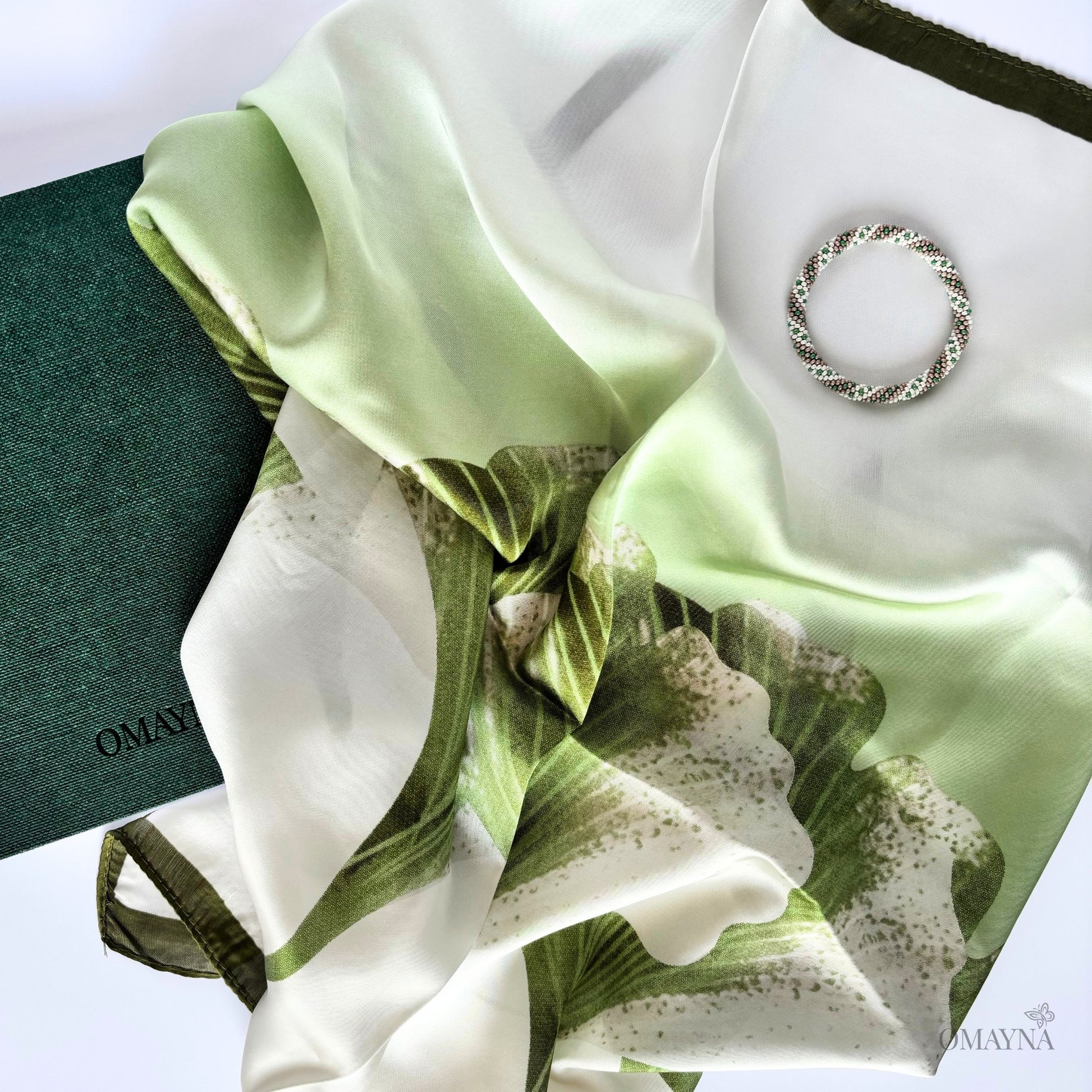 Green and white floral silk scarf with a bracelet and notebook on a white background