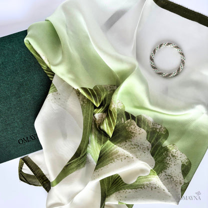 Green and white floral silk scarf with a bracelet and notebook on a white background
