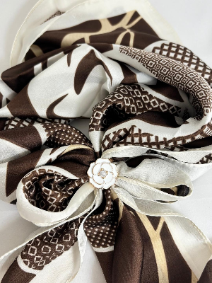 Brown and white patterned scarf with a decorative bow on a white background