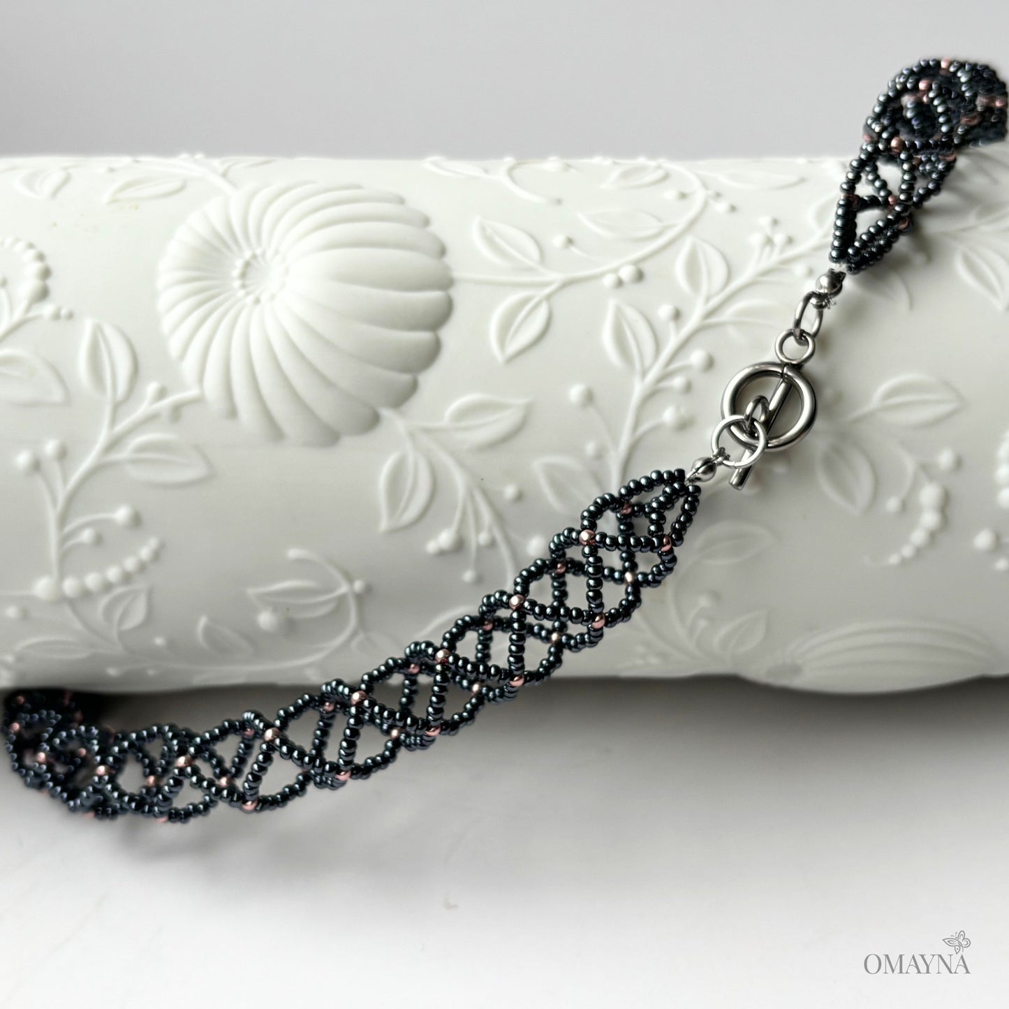 Close-up of Sofia beaded necklace in hematite & copper rose on a decorative element