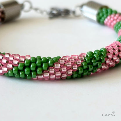 Close-up of a beaded bracelet in Green and Pink with a clover charm on a white background