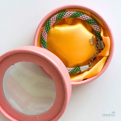 Open pink jewellery box with a yellow base in green and pink beads on a white background